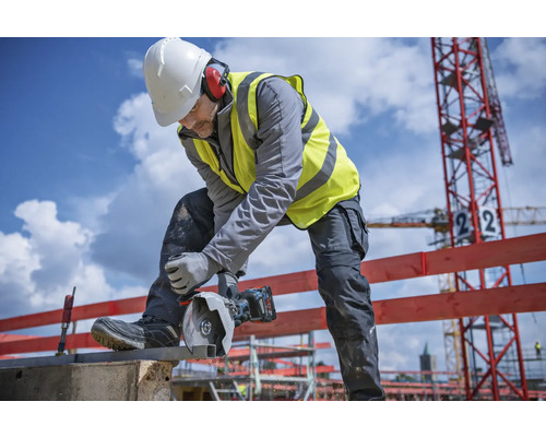 Ein Bauarbeiter schneidet mit einer Trennschleifmaschine ein Metallstück auf einer Baustelle.