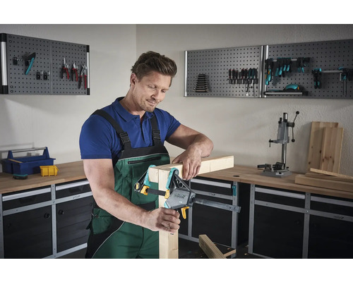 Mann befestigt Holz mit einer Schraubzwinge in einer Werkstatt.