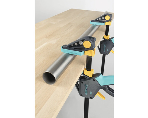 Werkstück mit Wolfcraft Einhandzwingen und einem Rohr an einer Tischplatte befestigt.