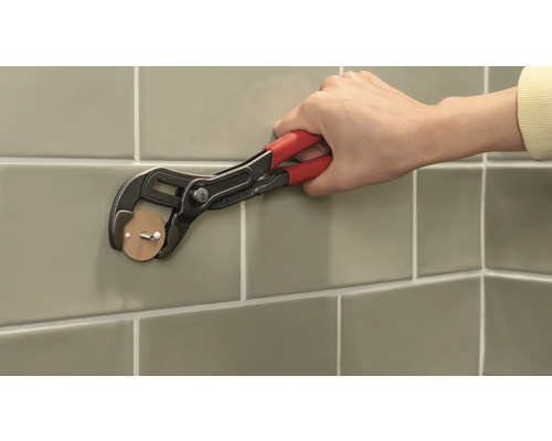 Person befestigt einen Klebehaken mit einer Rohrzange an einer gefliesten Wand.