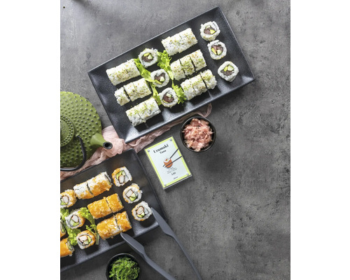 Zwei Platten Uramaki Sushi, Ingwer, Algen und eine Teekanne auf einem Tisch