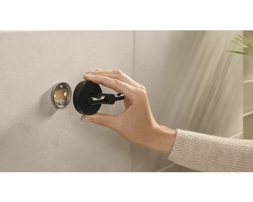 Eine Hand montiert einen schwarzen Doppel-Kleiderhaken an einer Wand.