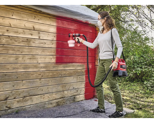 Frau streicht Holzwand mit Farbsprühsystem rot