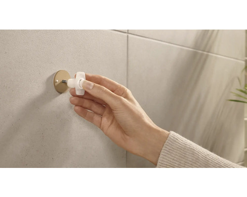 Eine Hand montiert einen Handtuchhaken an einer gefliesten Wand