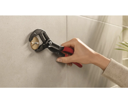 Eine Person befestigt einen Klebehaken mit einer Rohrzange an der Wand.