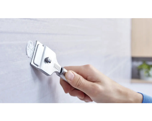 Eine Hand verwendet einen Glasschaber zum Entfernen von Materialresten von einer Fliese.