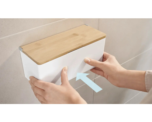 Aufnahme einer Person, die eine weiße Kosmetiktuchbox mit Bambusdeckel an der Wand befestigt.