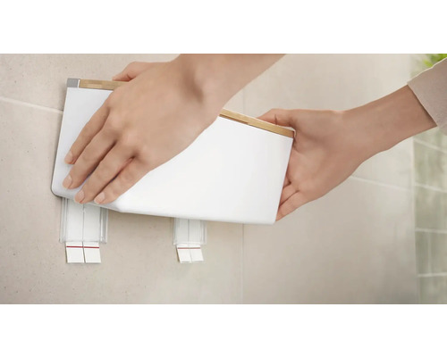 Person befestigt einen weißen Wandseifenspender mit Bambusdeckel an der Wand