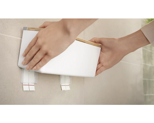 Eine Person befestigt einen weißen Papierhandtuchspender mit Bambusdeckel an der Wand.