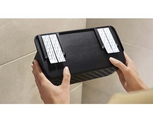 Person befestigt schwarzen Wandlüfter mit Klebestreifen an der Wand