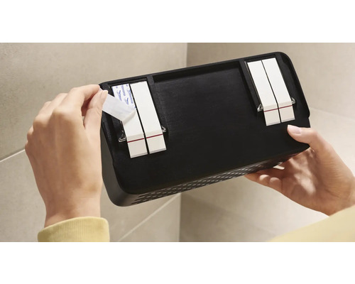 Person befestigt ein schwarzes Wandregal mit Klebestreifen an einer Wand