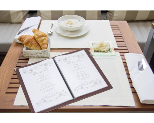 Ein gedeckter Tisch mit Speisekarte, Croissants, Suppe und Beilage.