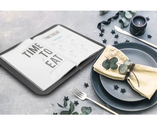 Szene mit einem geöffneten Menübuch, Tellern, einer Serviette und Besteck auf einem Tisch