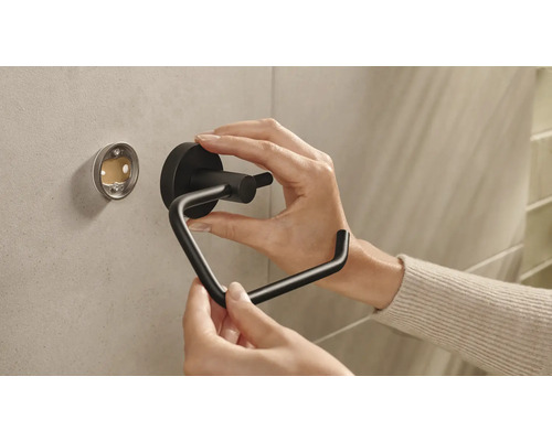 Eine Person montiert einen schwarzen Toilettenpapierhalter an einer Wand.