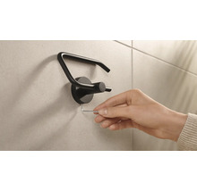 Eine Hand montiert einen schwarzen Toilettenpapierhalter mit einem Inbusschlüssel an einer Wand.