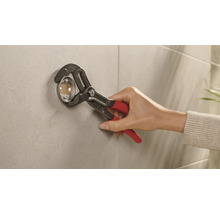 Installateur befestigt mit einer Rohrzange eine Rosette an einer Wand