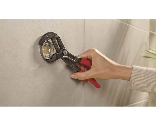 Installateur befestigt mit einer Rohrzange eine Rosette an einer Wand