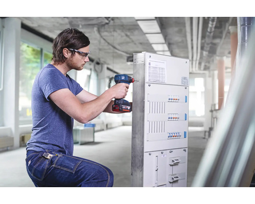 Elektriker mit Akku Bohrschrauber vor Verteilerkasten