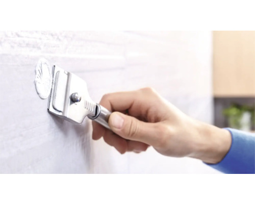 Eine Hand verwendet einen Fliesenfugenentferner, um Mörtel von einer Fliese zu entfernen.