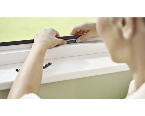 Person montiert ein Insektenschutzgitter an einem Fenster