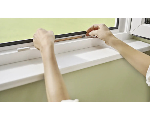 Eine Person misst mit einem Bleistift die Dichtung eines Fensters.