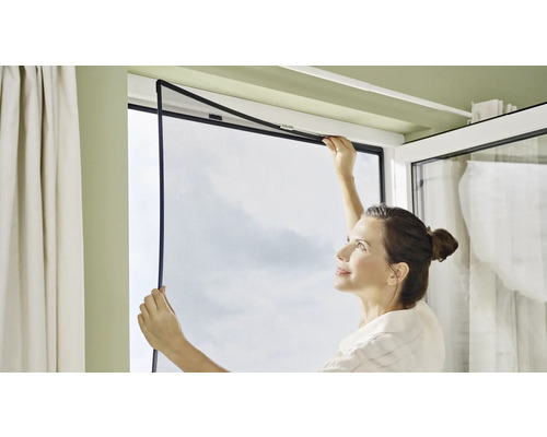 Frau montiert ein Insektenschutzgitter am Fenster.