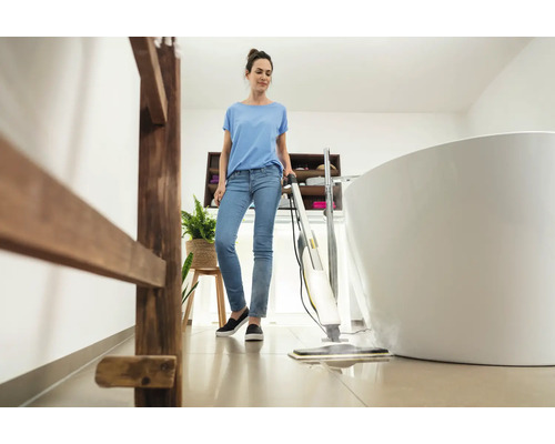 Frau reinigt Boden mit Dampfreiniger in hellem Badezimmer mit Badewanne