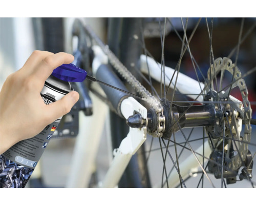 Eine Person schmiert die Kette eines Fahrrads mit einem Kettenspray.