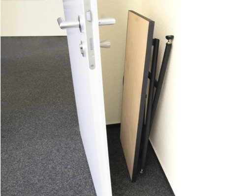 Zusammengeklappter Klapptisch mit schwarzem Gestell an einer Wand stehend