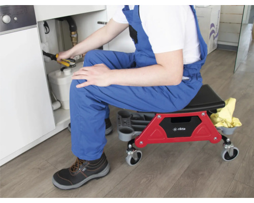 Ein Installateur sitzt auf einem Werkstattrollhocker während er unter einem Waschbecken arbeitet.