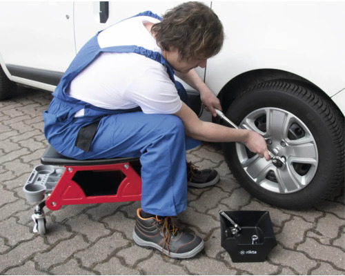 Mechaniker wechselt mit Werkstatthocker und Drehmomentschlüssel einen Reifen an einem Kraftfahrzeug