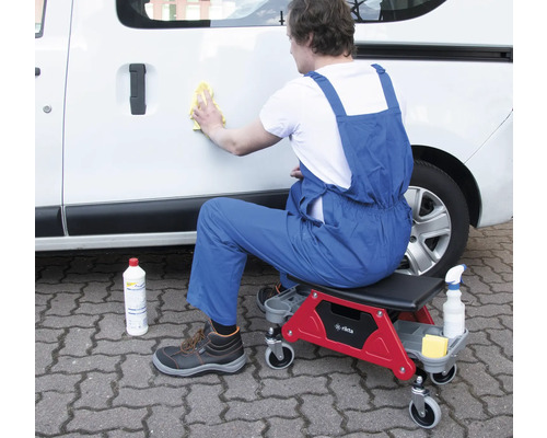 Mann reinigt Auto mit Werkstatthocker und Reinigungsmittel