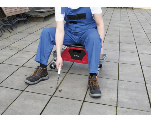 Person auf einem Werkstatthocker beim Entfernen von Unkraut zwischen Pflastersteinen