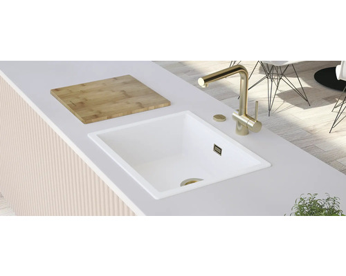 Küchenszene mit weißem Spülbecken, goldener Armatur und Holzschneidebrett auf einer Arbeitsplatte.