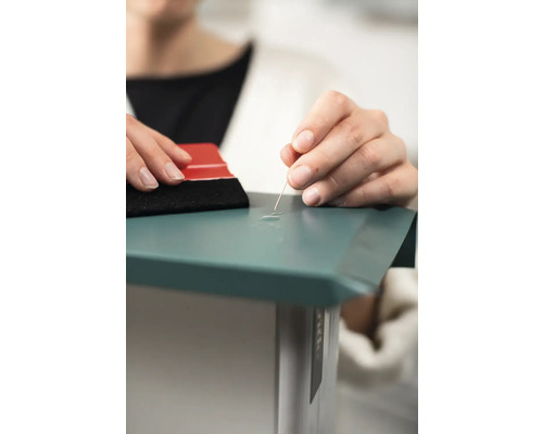 Eine Person verwendet eine Nadel und einen Rakel, um Luftblasen unter einer Folie zu entfernen.