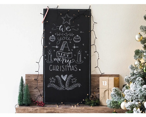 Dekorative Tafel mit Weihnachtswünschen, Lichterkette, Weihnachtsbaum und Geschenken für eine festliche Atmosphäre