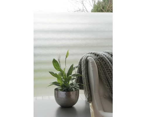 Friedenslilie in einem Metalltopf auf einem Tisch, neben einem Sessel mit einer Strickdecke.