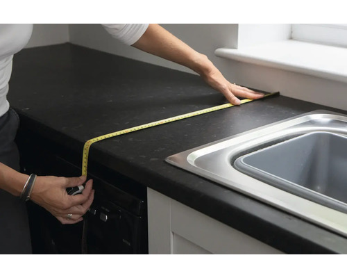 Person misst eine Küchenarbeitsplatte mit einem Bandmaß.