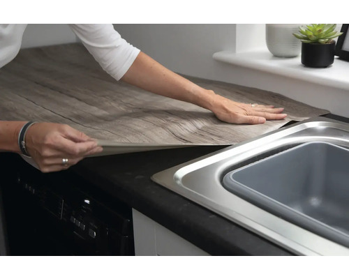 Frau bringt Dekorfolie in Holzoptik auf Küchenarbeitsplatte an