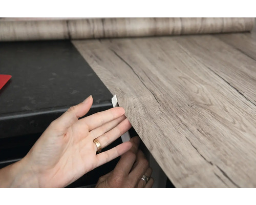 Anbringen einer selbstklebenden Folie mit Holzoptik auf einer Oberfläche