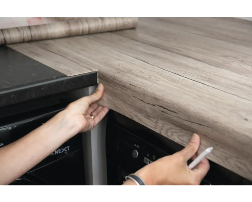 Person bringt eine Klebefolie mit Holzoptik auf einer Küchentheke an.