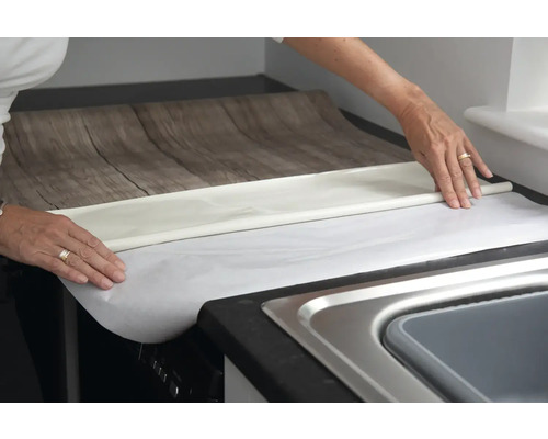 Person verlegt Möbelfolie mit Holzoptik auf einer Arbeitsplatte in der Küche.