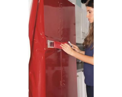 Frau bringt Folie mit Rakel und Messer an Kühlschrank an