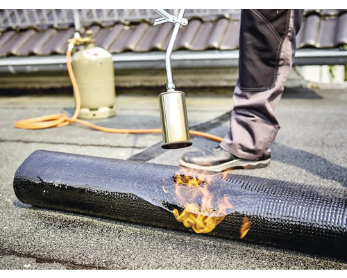Ein Handwerker verschweißt mit einem Gasbrenner eine Dachbahn.