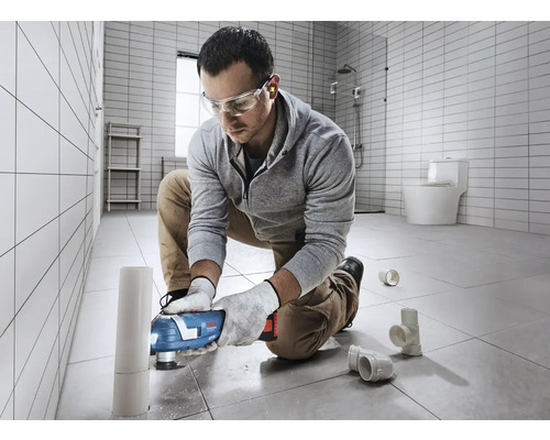 Mann arbeitet mit einem Multifunktionswerkzeug an einem Rohr im Badezimmer