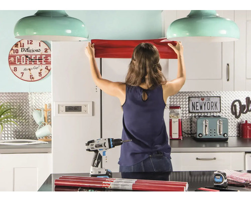 Frau befestigt Möbelfolie in einer Küche mit Werkzeug.