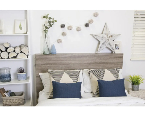 Schlafzimmer mit Bett, Kopfende aus Holz, Kissen und dekorativen Elementen wie Lichterkette und Holzstern
