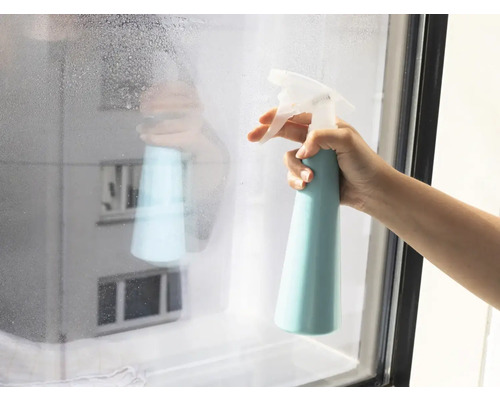 Eine Hand sprüht Reiniger auf ein Fenster