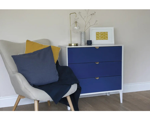 Wohnzimmerszene mit Sessel, Kissen, Tagesdecke und Kommode mit Lampe und Dekoartikeln