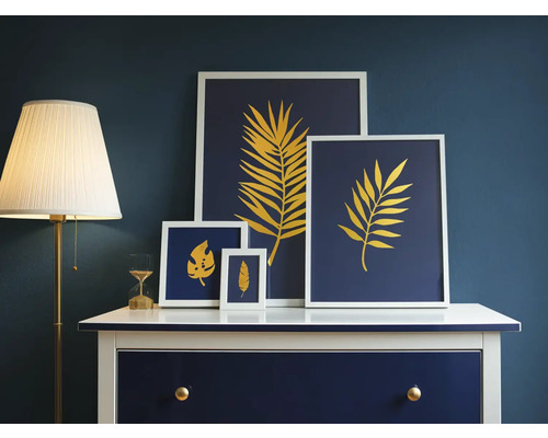 Dekorative Bilder mit Blattmotiven auf einer Kommode mit Lampe